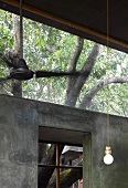 Simple pendant lamp in front of concrete wall with transom and view of tree
