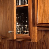 Detail of a fitted walnut cupboard with an open door an a glimpse of glasses