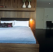 A double bed with a wooden frame in front of a wood panelled partition wall