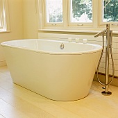 A white free-standing bath tub with a designer floor tap on light wooden floor boards
