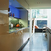 A modern fitted kitchen with shiny cupboards and coloured lights behind a glass wall