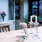 Kleine Glasvasen mit Rosen und Kerzen auf einem Tisch
