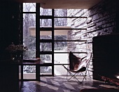A bat-wing chair in front of floor-to-ceiling windows in an anteroom in a rustic house