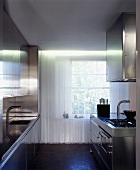 Cord curtain in front of lattice window in minimalist stainless steel kitchen with two worktops