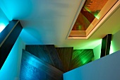 Holzblenden mit indirektem, farbigem Licht als Geländer an gewendelter Holztreppe und Blick durch Innenfenster