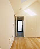 View of doors in white walk-in closet with light wooden floorboards and sun falling through skylight