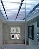 Modern bathroom with view of neighbouring house through English sash window and horizontal skylight with sunshade