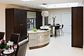 Designer kitchen with curved kitchen island and dark brown wooden cupboards in open-plan dining room