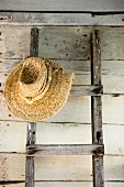 Ladder with straw hat leaning on wooden wall