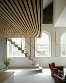 Living room in villa with leather armchairs under gallery and light metal staircase in front of arched windows