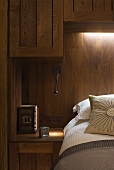 Bed in front of wood-clad wall with indirect lighting and wooden wall cupboards
