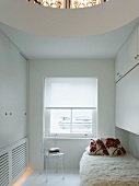 White guest bedroom with circular opening in ceiling above bed with flokati blanket and plain fitted cupboards