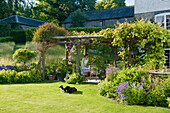 Überdachte Pergola im grünen Garten mit Blumen und Hund