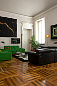 Wohnzimmer mit Parkettboden, schwarzer Ledercouch und grüner Couch