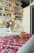 Modernes Schlafzimmer mit Wandregal, floraler Tagesdecke und kleinem Holztisch mit Gebäck