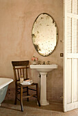 Holzstuhl und antiker, ovaler Spiegel im Vintage-Badezimmer