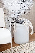 Black and white rag dolls lying on metal bin in front of painting on fabric and armchair on knitted rug