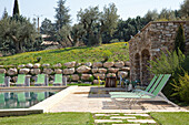 Poolbereich mit Liegestühlen und Steinmauer in mediterraner Gartenlandschaft