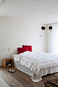 Minimalistisch gestaltetes Schlafzimmer mit weißer Bettwäsche und rotem Kissen