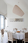Helles Esszimmer mit weißem Tisch, klassischen Stühlen und Designerlampe