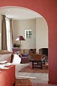 Wide arched doorway in dining room wall painted dusky pink with view of open fireplace in living room