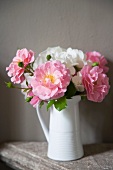 Bouquet of white and pink roses in vintage china jug against grey wall