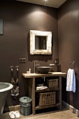 Badezimmerecke mit rustikalem Waschtisch und aufgesetzter Keramikschüssel neben Designerarmatur unter Wandspiegel an dunkelgrau getönter Wand