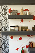 Wall shelves with decorative objects in front of patterned wallpaper with red accents