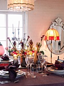 Gedeckter Tisch mit festlicher Kerzen- und Blumendekoration; eine Stehlampe mit gelbem Lampenschirm sorgt zusätzlich für warmes Licht