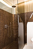 Reflections on tinted glass screen of floor-level shower with copper-coloured, iridescent mosaic tiles