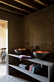 Stilmix im Badezimmer mit verzinkten Waschschüsseln vor rustikaler, schlammfarbener Wand und modernen Wandarmaturen