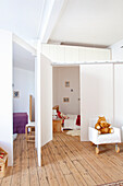 Hell gestaltetes Kinderzimmer mit Trennwänden, weißem Sessel und Stofftier