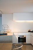 Minimalistische Küche mit weißen Fronten, Beleuchtung und integriertem Ofen