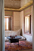 Besondere Wandgestaltung und Fensterumrahmung in orientalisch eingerichtetem Raum mit Bodenkissen und Tablett-Tisch auf buntem Teppich