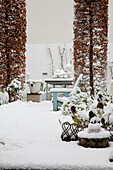 Verschneiter Gartenbereich mit Sitzbank und Pflanzgefäßen im Winter