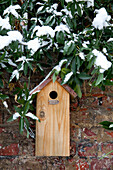 Vogelhaus aus Holz an einer Ziegelmauer mit schneebedeckten Zweigen
