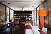 Open-plan dining and living room with orange standard lamp in front of floor-to-ceiling windows with closed blinds