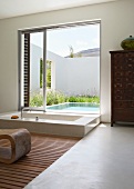Modern, exotic luxury bathroom - sunken bathtub in front of open sliding terrace door with view of pool in courtyard