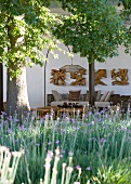 Sunny mood - seating area with designer lamp and wood sculptures, Tree and flowerbed in foreground