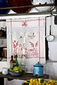 Detail of kitchen; embroidered tea towel in front of niche below vintage pan lids on wall rack