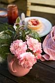 Kleiner Gartenstrauss mit Rosen in rosa Kännchen auf Frühstückstisch