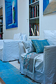 White armchairs, decorative cushions, patterned blanket and bookcase