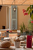 Terrasse mit Bambusmatten auf leichter Pergola-Konstruktion, mediterrane Pflanzen und gedeckte Tische; Muscheldekoration im Vordergrund
