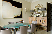 Dining room with glass table, grey chairs and large abstract painting on the wall