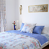 Bed with floral bed linen, picture and figurine on the wall