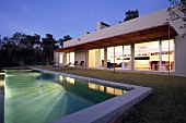 Hell erleuchtete Innenräume eines modernen Landhauses mit großem Swimmingpool und sich spiegelndem Licht