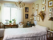 Simple single bed in bedroom with pictures on wall and antique wooden furniture