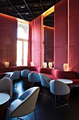 Venetian hotel lounge with small leather armchairs and meandering, red plush sofa against wall with upholstered panels
