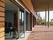 Terrassenplatten aus Holz an Haus im grosszügigen 60er Stil mit Betonauskragung auf Stützen und Holzverkleidung über Fensterfront
