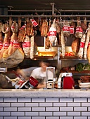 Sausages and hams on butcher's hooks above tiled counter in English shop